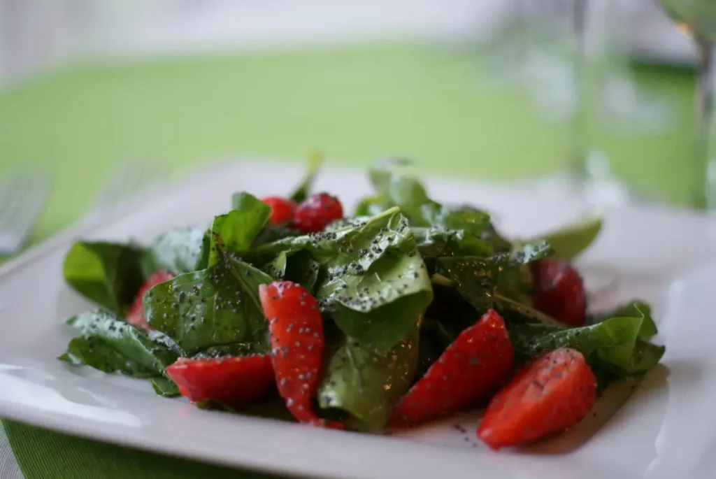 Variedad de alimentos antiinflamatorios, incluyendo brócoli, espinacas, fresas, cúrcuma, jengibre y almendras, organizados en platos y recipientes de madera.