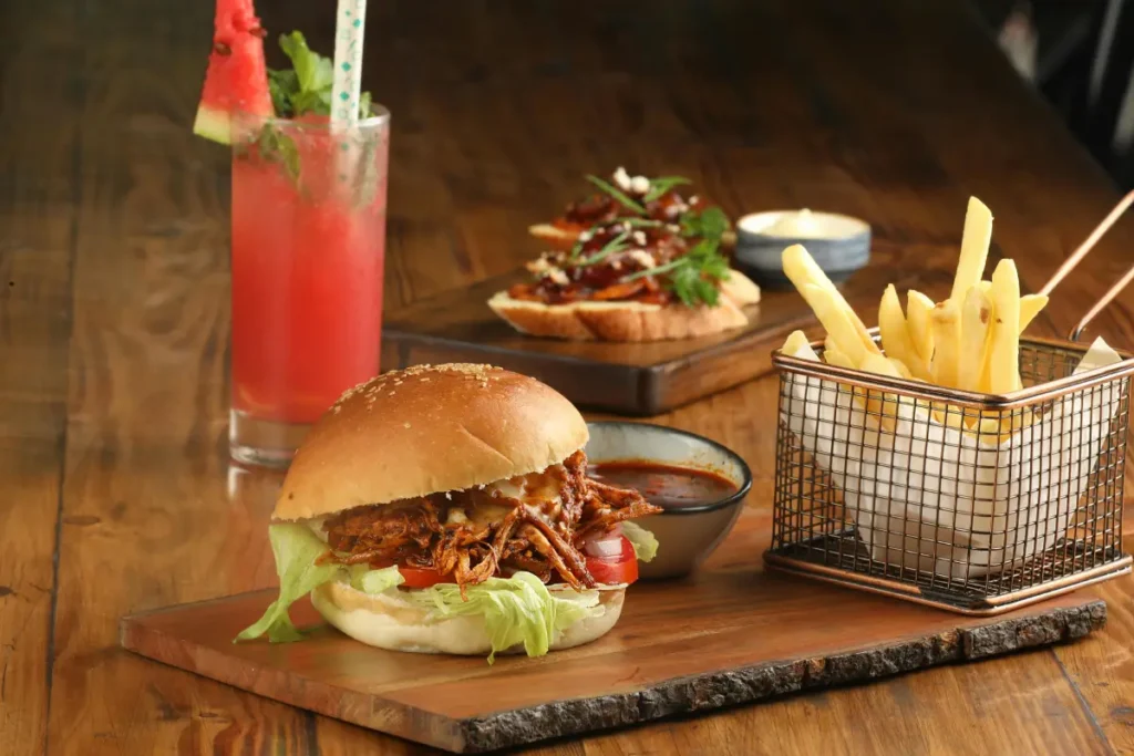 Alimentos procesados como hamburguesas, papas fritas, dulces y refrescos colocados en una mesa, representando productos que pueden generar inflamación en el cuerpo.