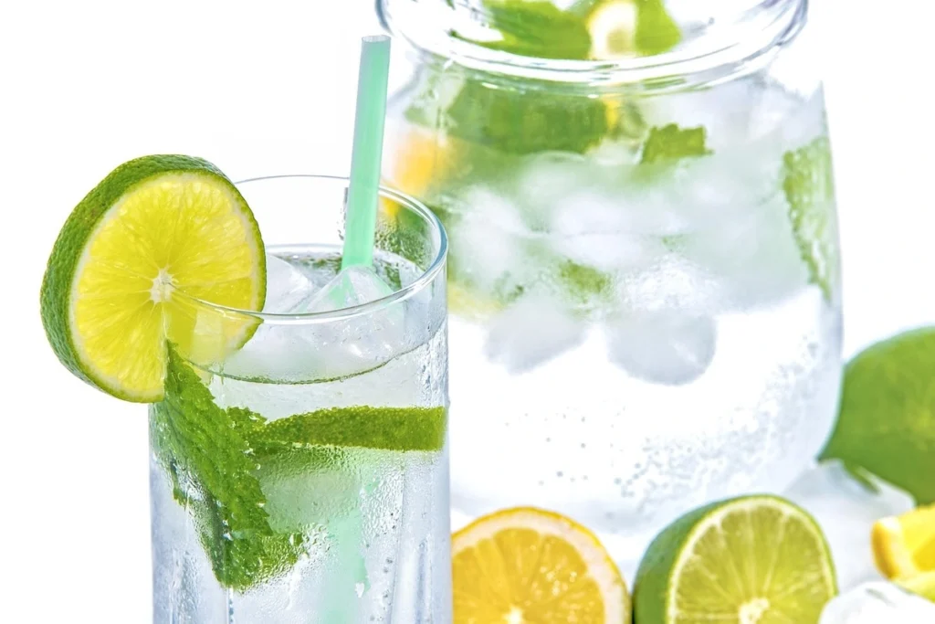 Vaso de agua con rodajas de limón y una botella de agua para representar la importancia de la hidratación.