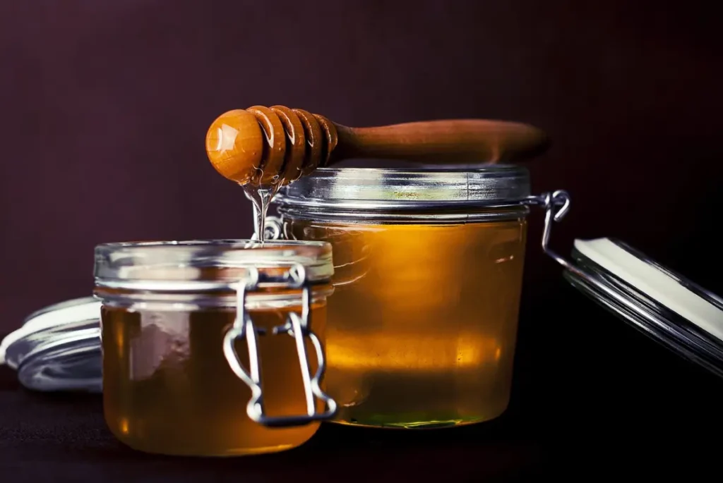 Miel en un tarro de vidrio con una cuchara de madera, usada como remedio natural para calmar la tos.