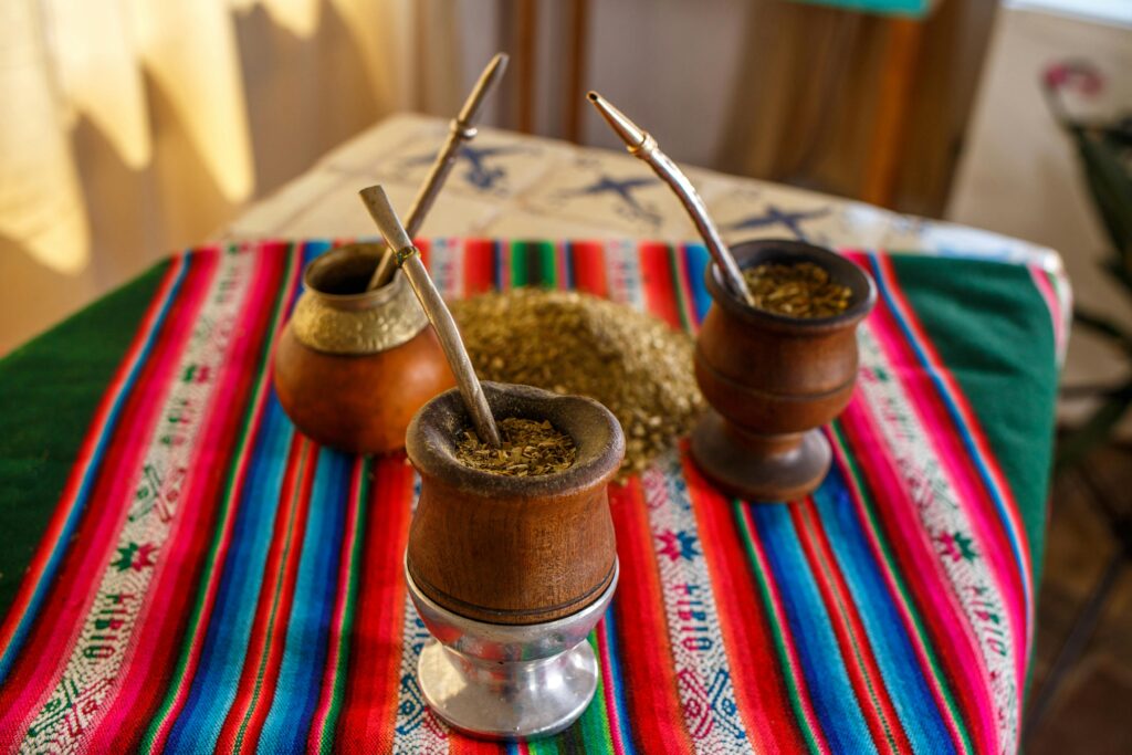 Una calabaza tradicional con bombilla llena de yerba mate sobre una mesa de madera en exteriores con vista a la naturaleza.