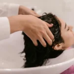 Mujer masajeando su cuero cabelludo con un tratamiento natural para eliminar la caspa.